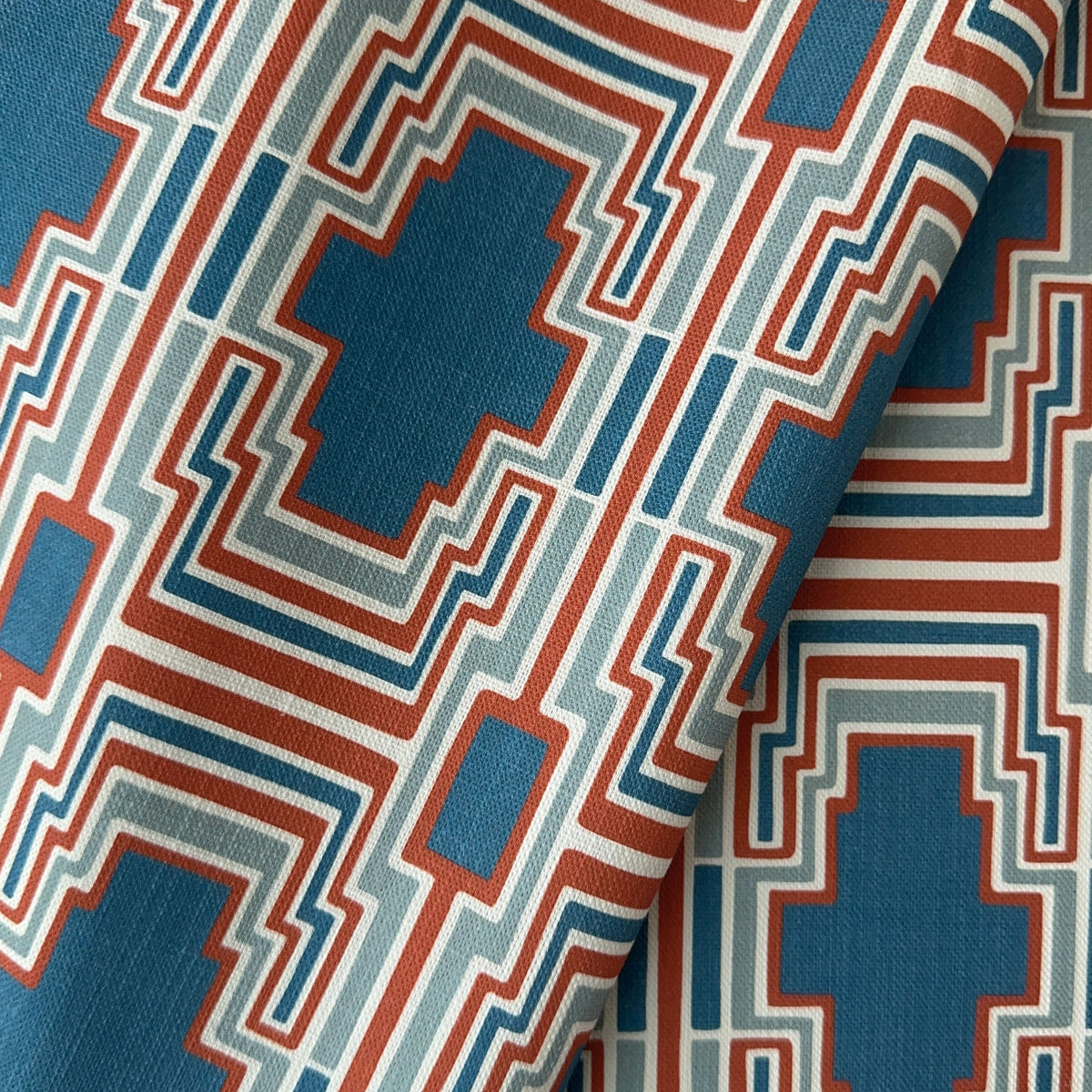 A close up of a geometric pattern with blue, terracotta, and ivory colours on a textured fabric background