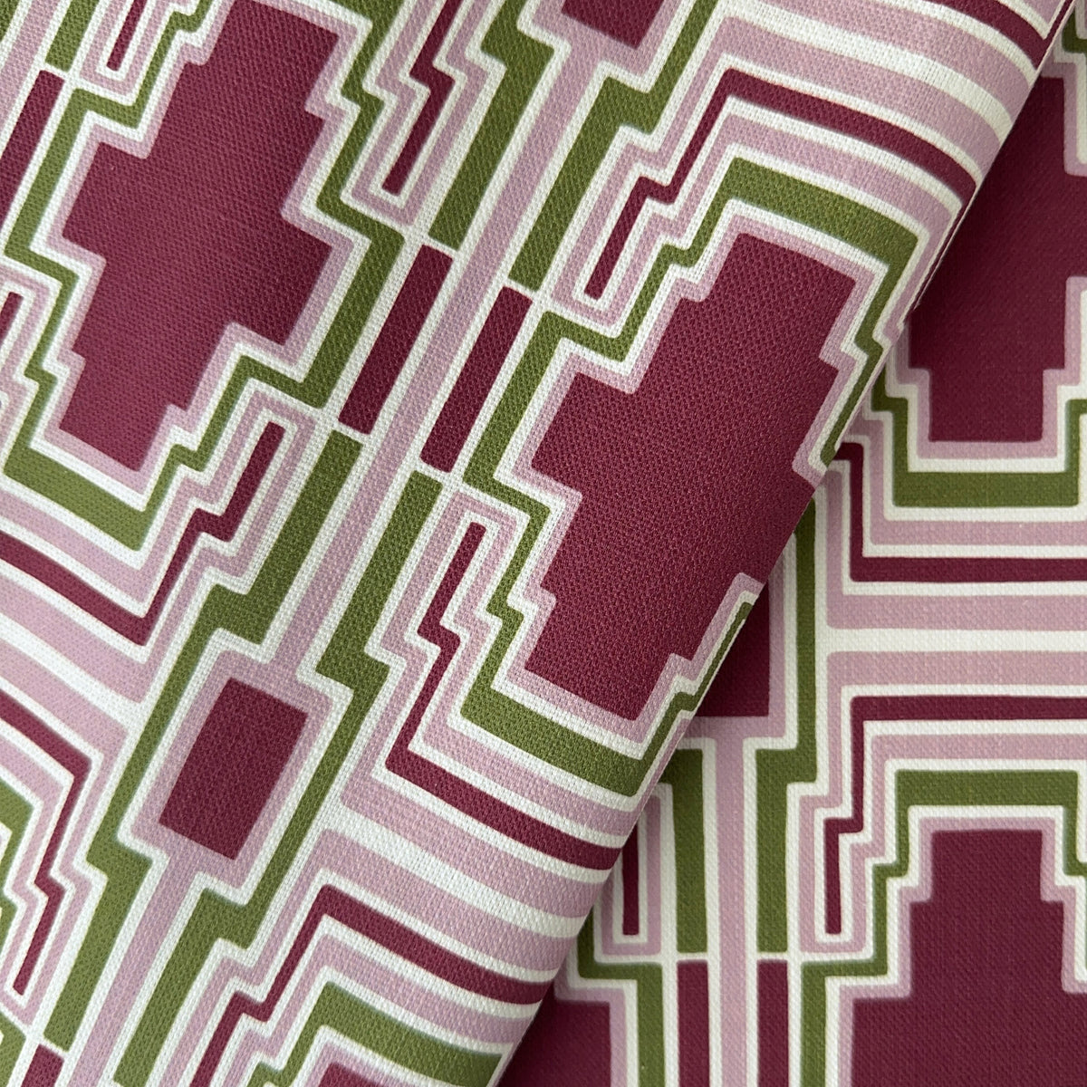 A close-up of a folded fabric with a geometric style pattern in burgundy, sage green, dusty pink, and ivory on a textured linen fabric
