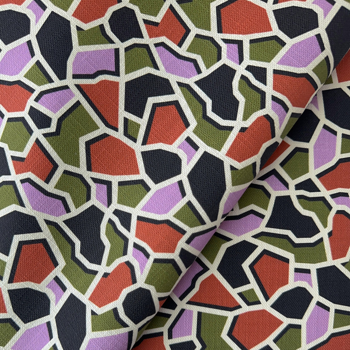 a close up of a geometric mosaic pattern with colorful green, lilac, terracotta and black shapes on a fabric background