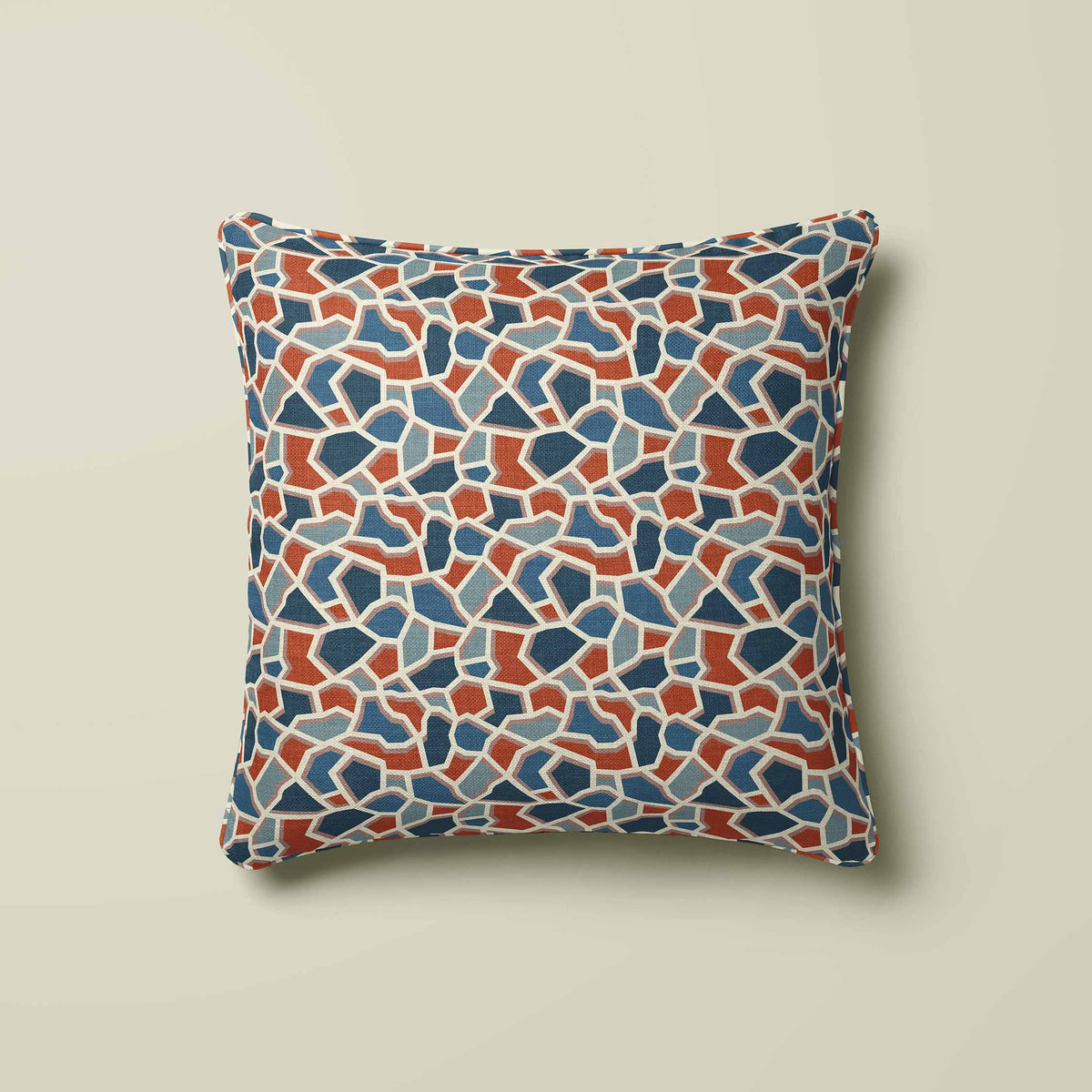 A square throw pillow featuring a terrazzo-style mosaic pattern in shades of blue, terracotta, and beige, set against a solid light beige background.