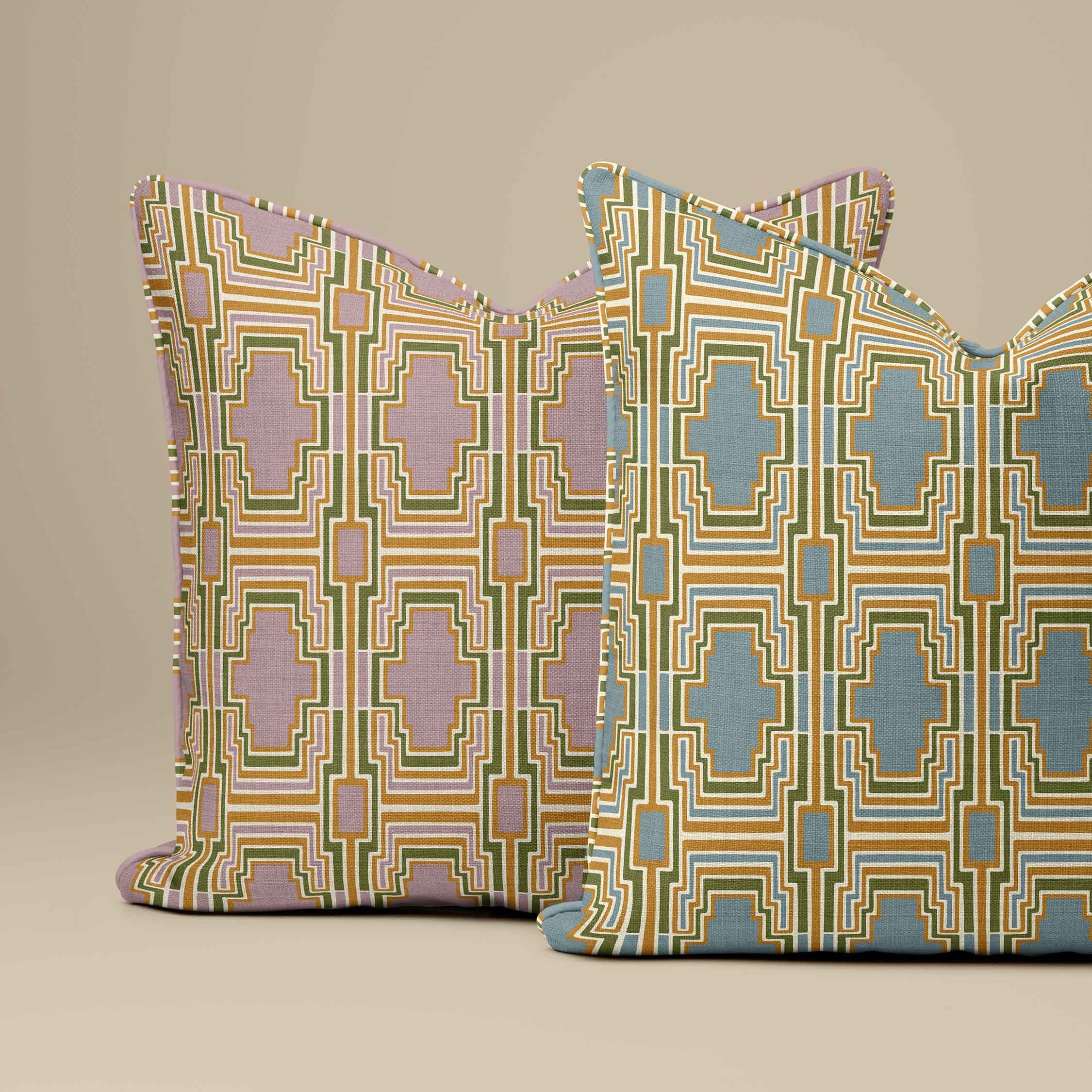 Two decorative throw pillows with a geometric pattern, featuring one in muted pink and olive green, and the other in blue and golden yellow, both with piped edges, set against a solid beige background.