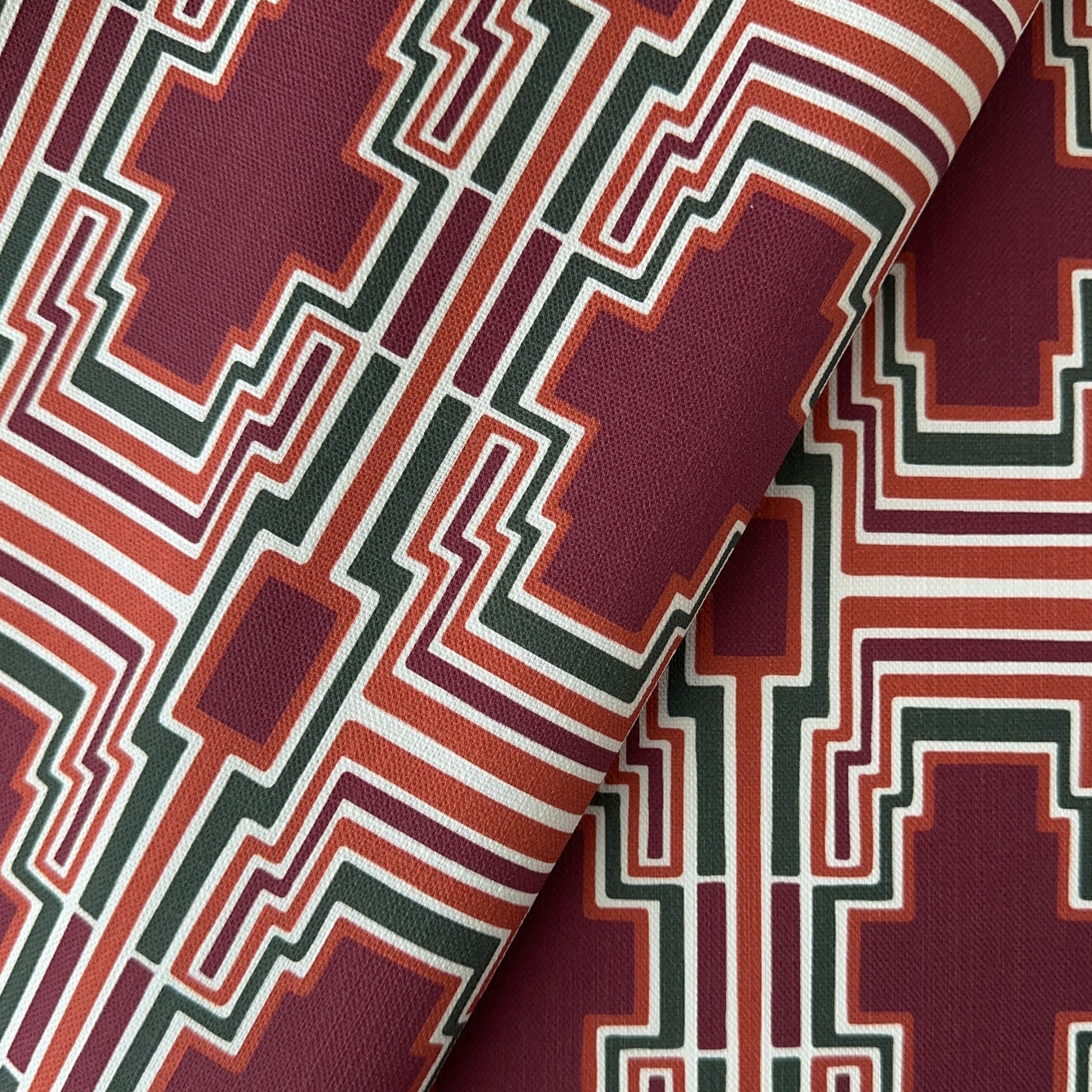A close up of a geometric pattern with terracotta, burgundy and green shapes on a fabric background