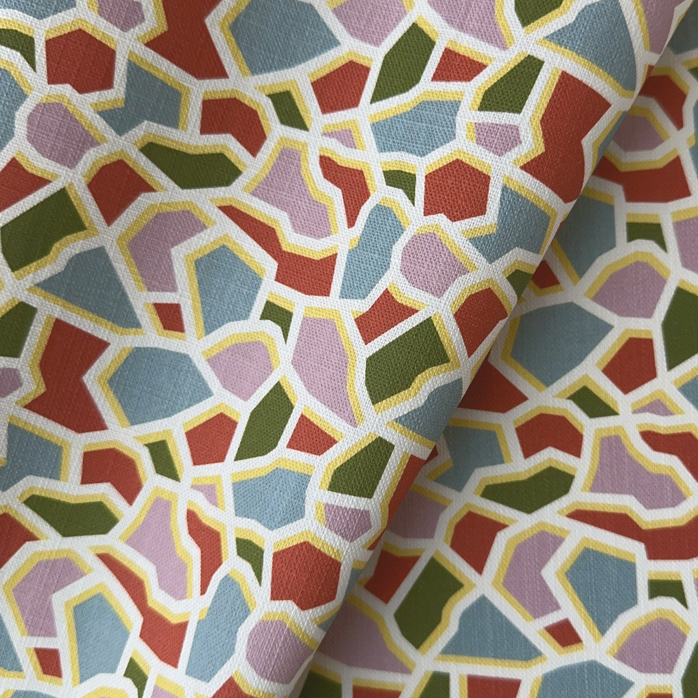 A close up of a printed geometric patterned fabric with terracotta green, and blue shapes on a multicolor background