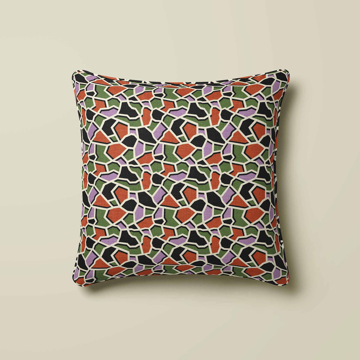 A square throw pillow featuring a colorful mosaic tile pattern in green, orange, purple, black, and white, set against a solid beige background.