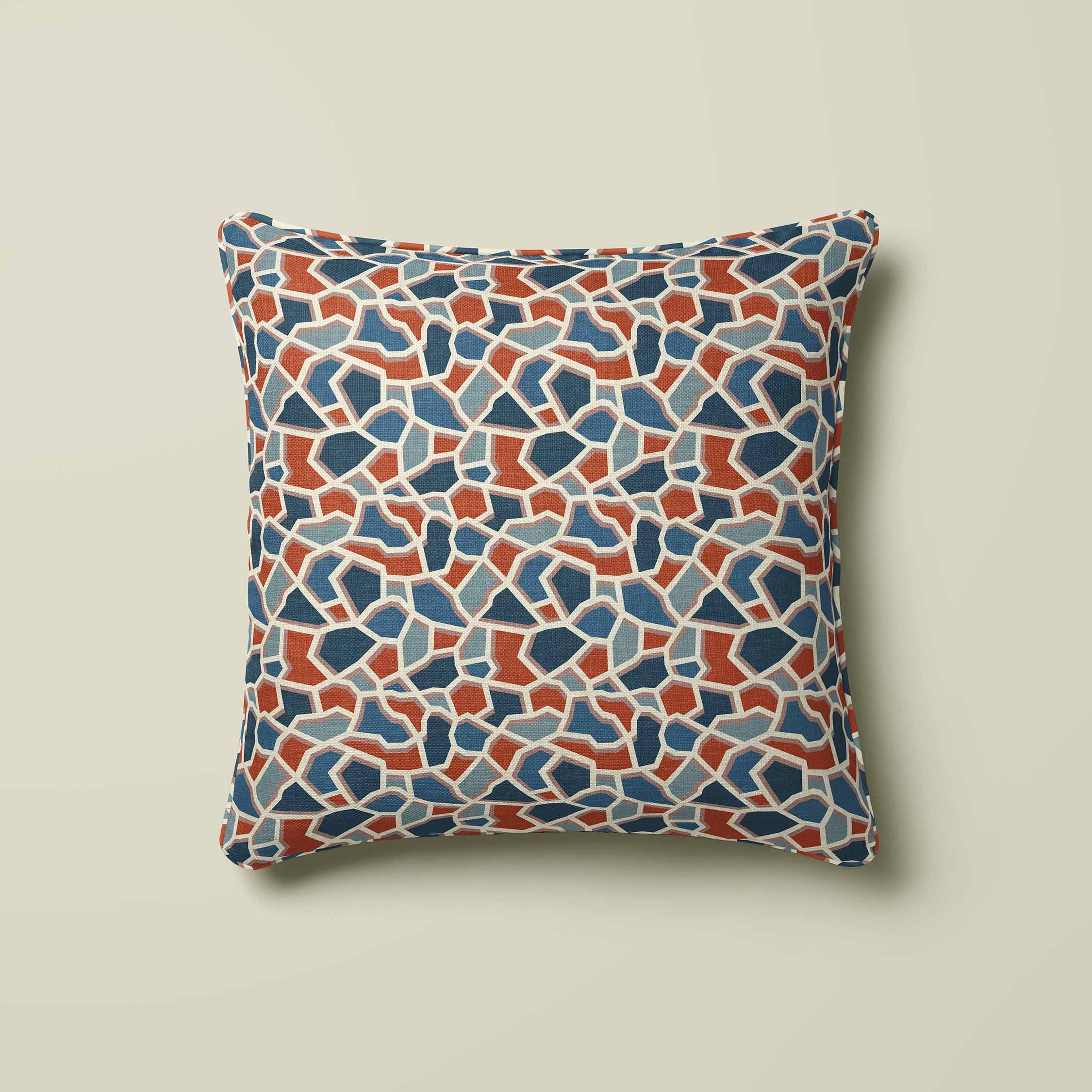 A square throw pillow featuring a terrazzo-style mosaic pattern in shades of blue, terracotta, and beige, set against a solid light beige background.